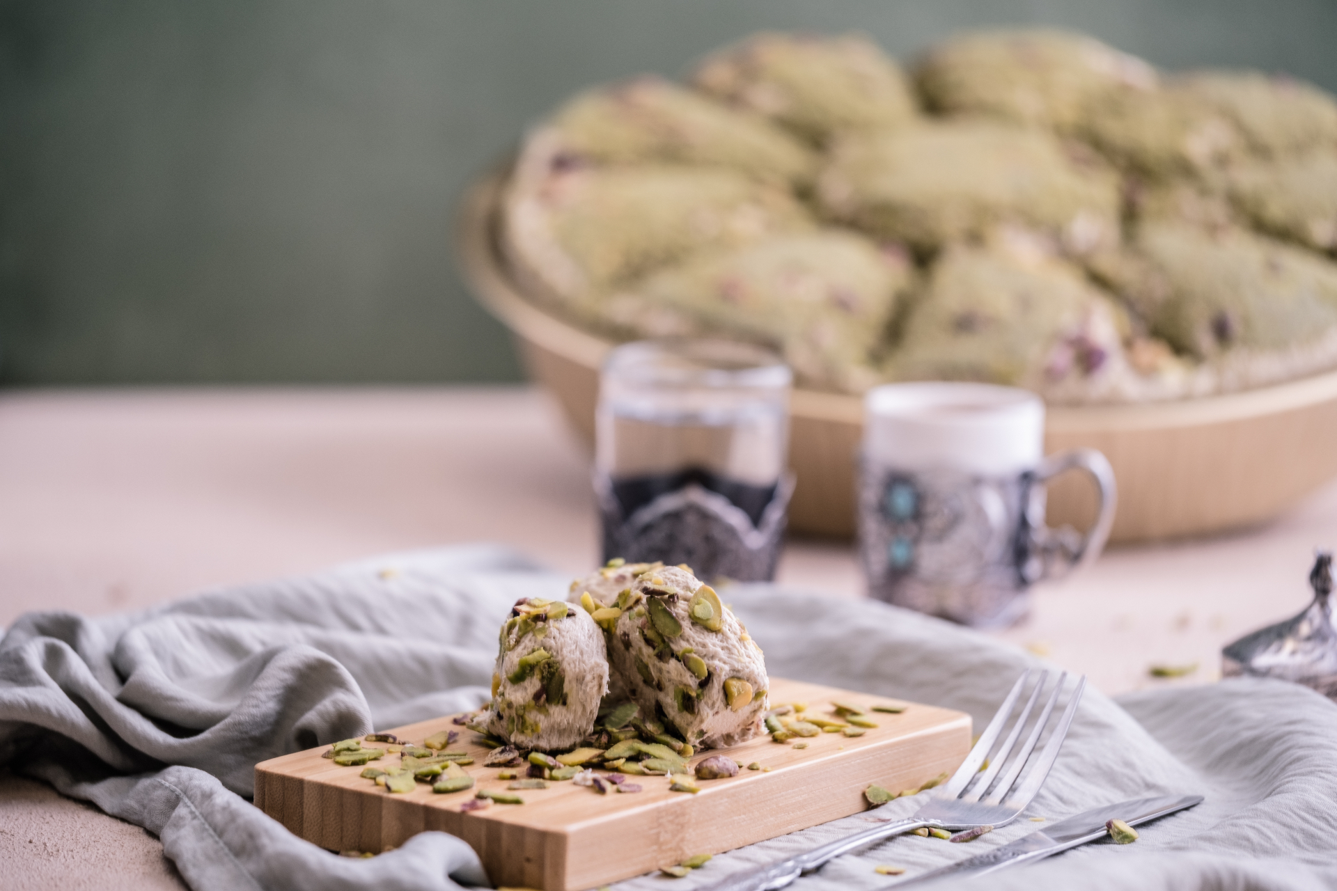 Lokum z prażoną pistacją na drewnianej deserce, w tle taca lokum z kruszoną pistacją